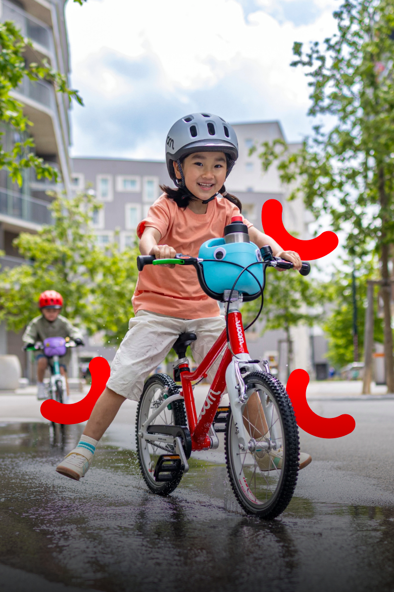 Smiling girl wearing a woom READY helmet riding a red woom GO bike with a blue POP bike basket.