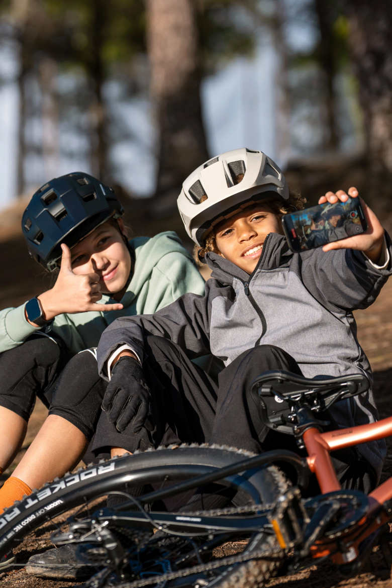 Two children with helmets taking a selfie next to a woom OFF MTB in the forest.