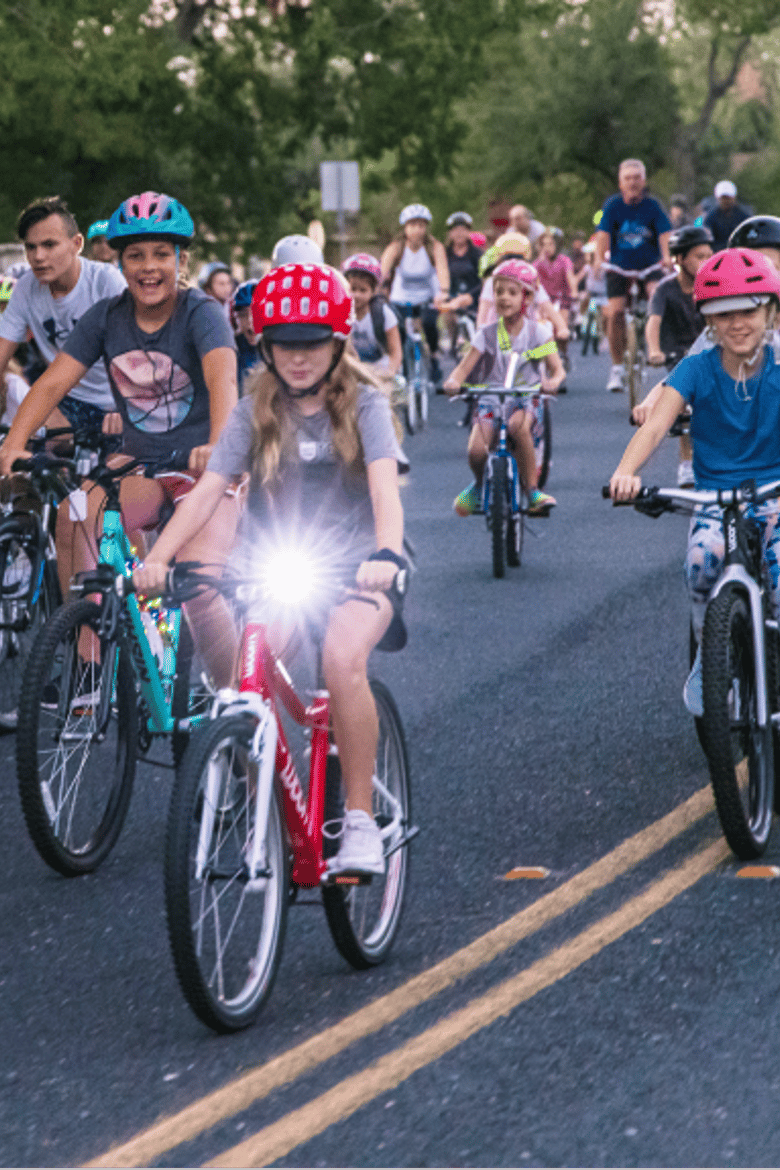 A crowd of children ride their bikes down an empty street in the early morning as they head to school with the Bike Bus program. A young girl on a woom bike leads the pack.