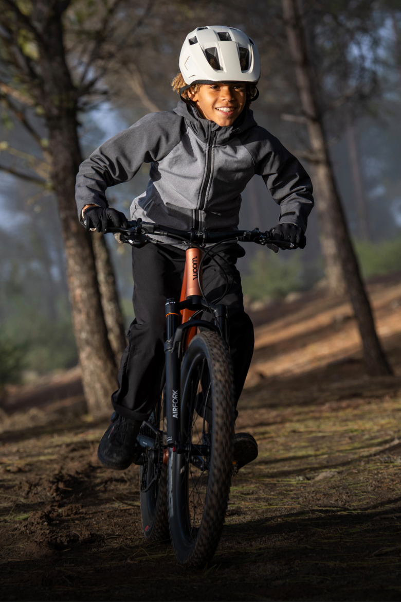 A person wearing a READY helmet rides a OFF mountain bike on a dirt trail through a forest.