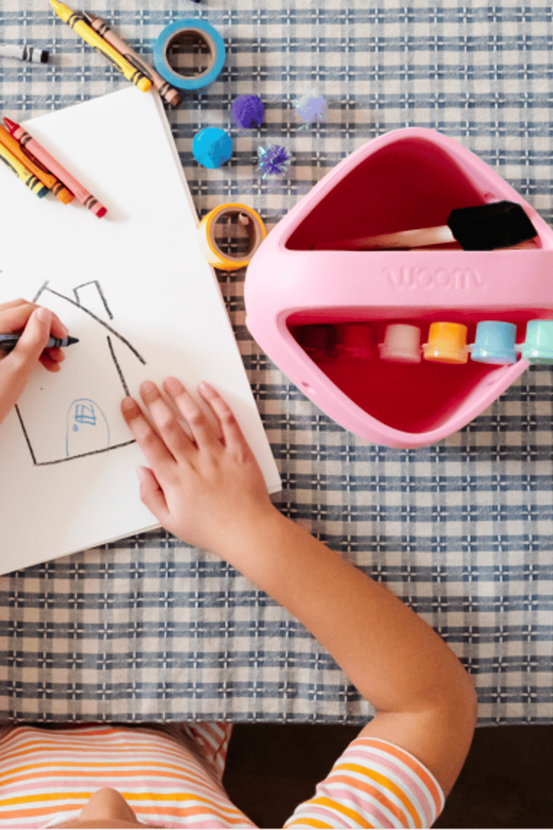 An overhead view of a child coloring next to a POP Basket filled with art supplies.