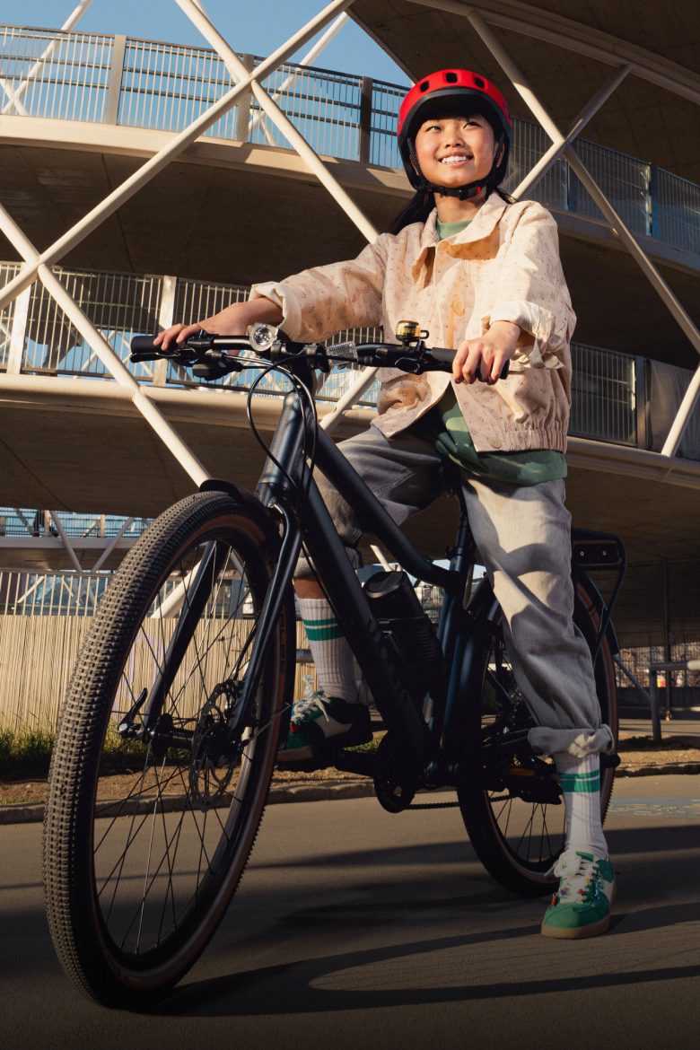 A person wearing a READY helmet on a black EXPLOREe e-bike outdoors in front of a modern structure.