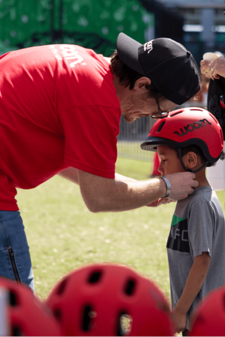 A woom employee helps fit a child with a correctly sized READY Helmet as he prepares to ride a bike at a local Austin event.