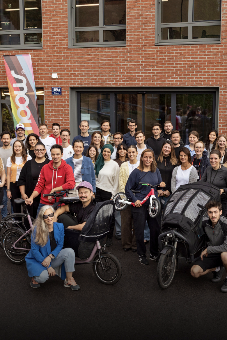 A large group of people posing with bicycles and a cargo bike in front of a brick building.