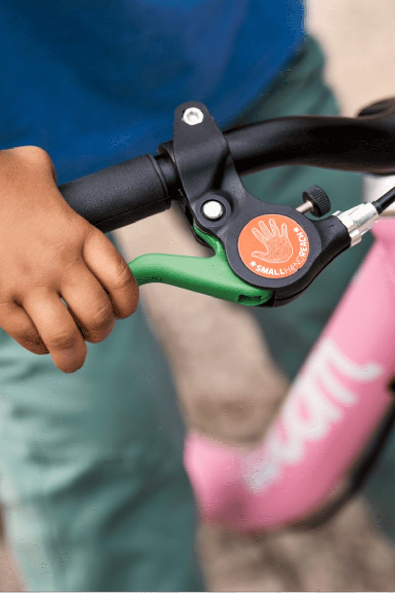 An overhead close-up view of a child’s hand squeezing the brake on a powder pink woom GO 1.