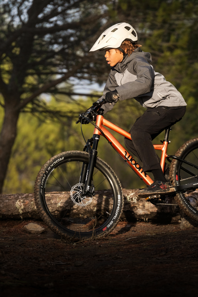 A boy riding a woom OFF mountain bike with focus through a sunny forest.