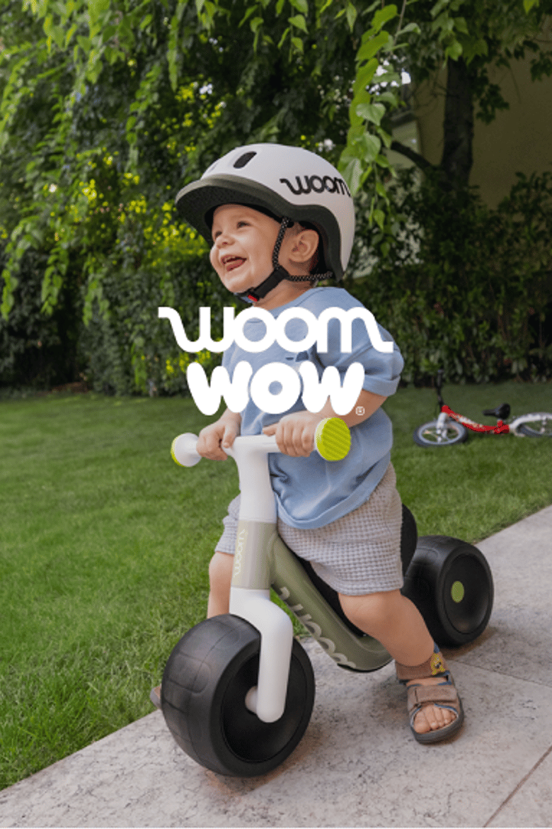 An image of a very young boy in a yard wearing a READY Helmet while riding a woom WOW in soft sprout.