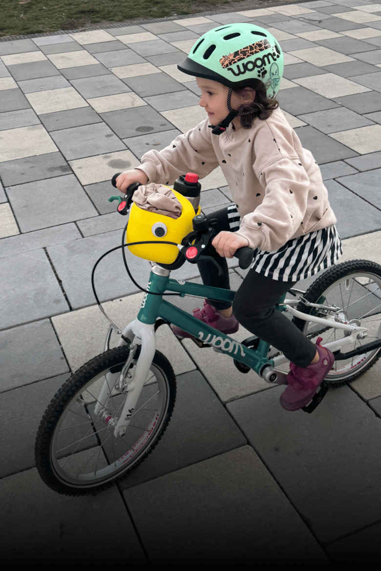 Kind mit grünem READY Helm fährt mit einem grünen woom GO bike, am Lenker ist ein gelber Fahrradkorb mit Wackelauge montiert