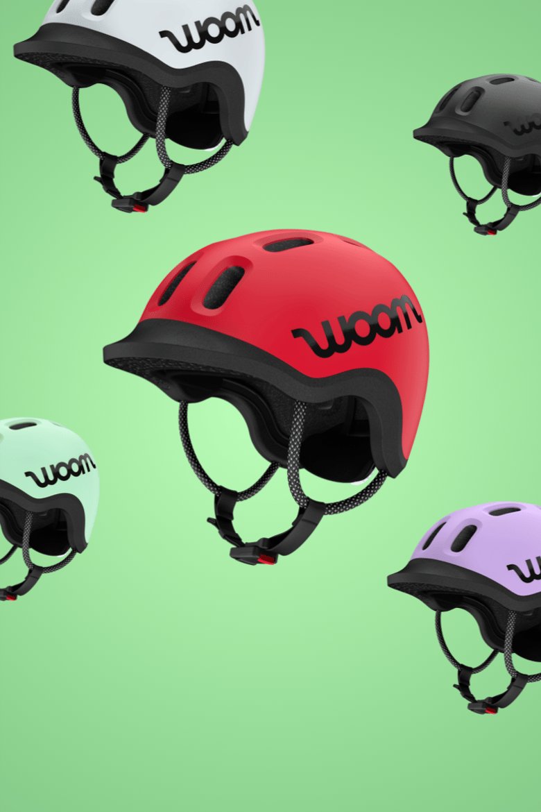 READY-fietshelmen van woom in de 5 kleuren woom red, mint, lilac, pale grey en charcoal metallic tegen een groene achtergrond