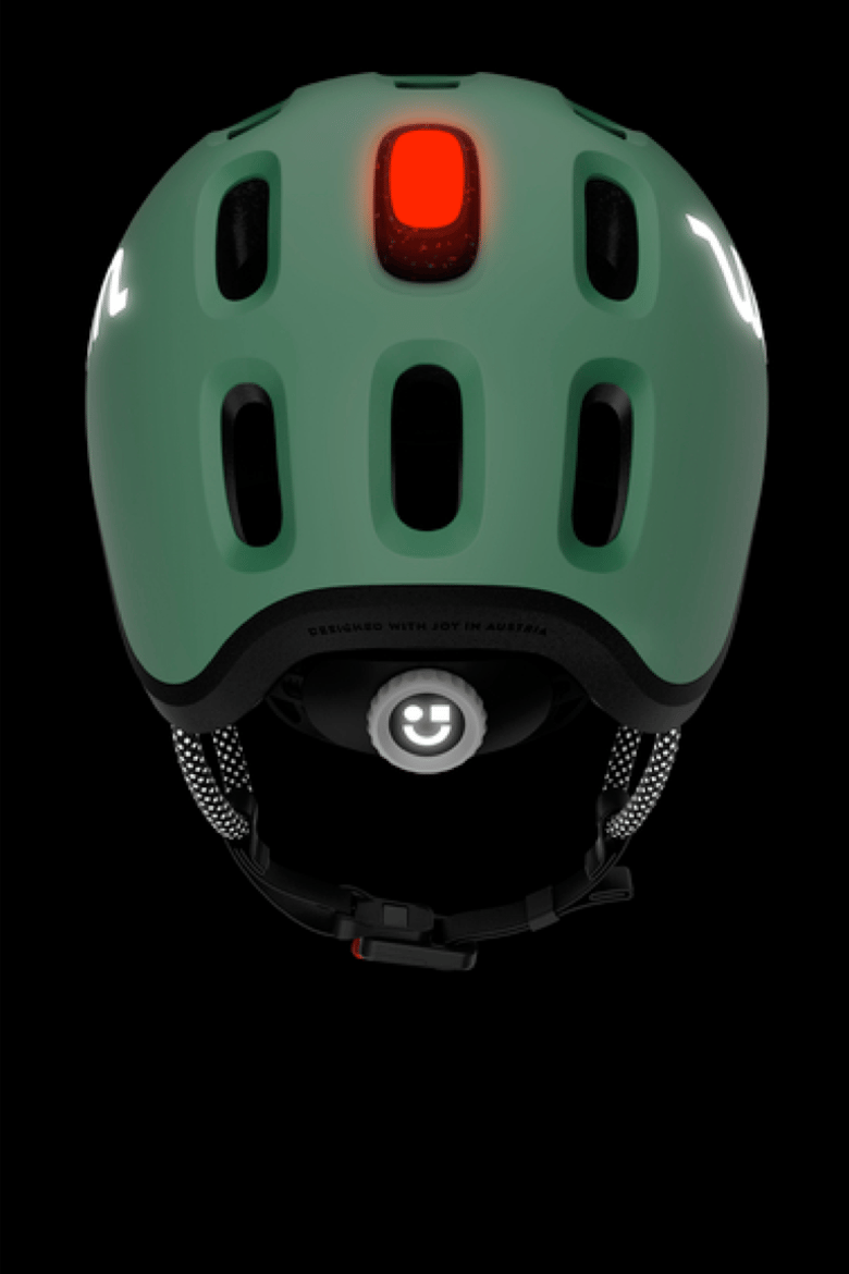 Donker achteraanzicht van de READY-kinderhelm in groen met daarin de rode helmlamp en reflecterende details