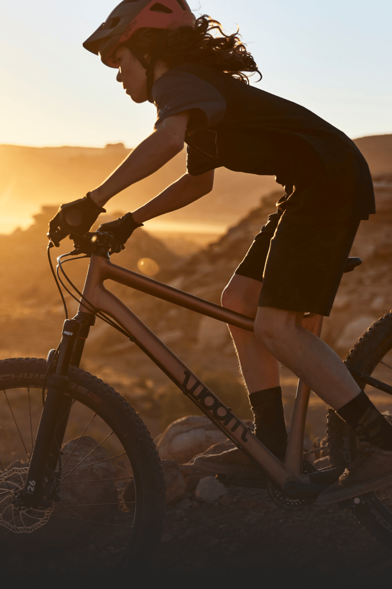 Kind met fietshelm op fietst bergaf in grondhouding op een woom OFF AIR mountainbike tijdens zonsondergang.