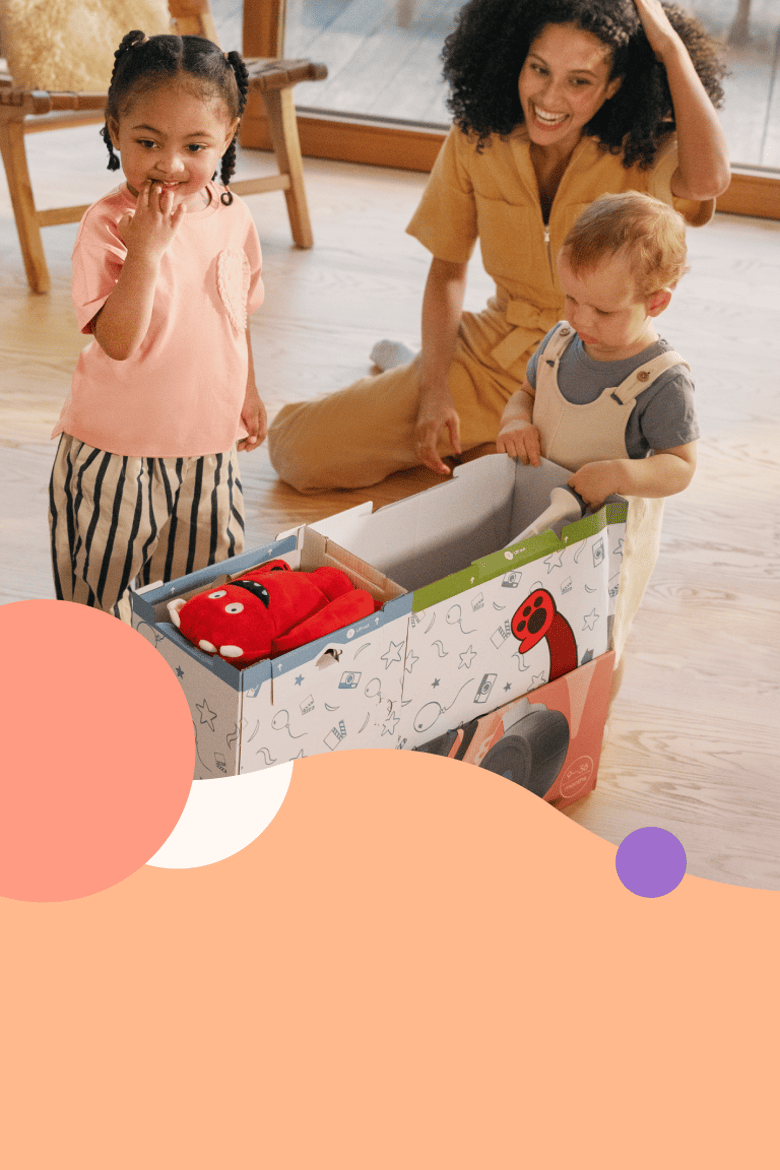 Två nyfikna småbarn packar upp woom WOW ur lådan. Den leende mamman sitter bakom dem.