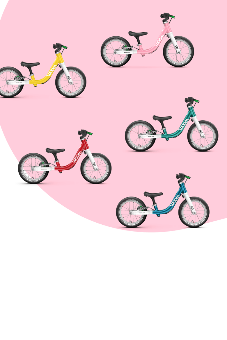 Five woom balance bikes in different colors on a pink background.