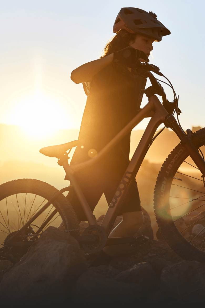 A teenager wearing a helmet is pushing his woom OFF mountain bike uphill as the sun sets.