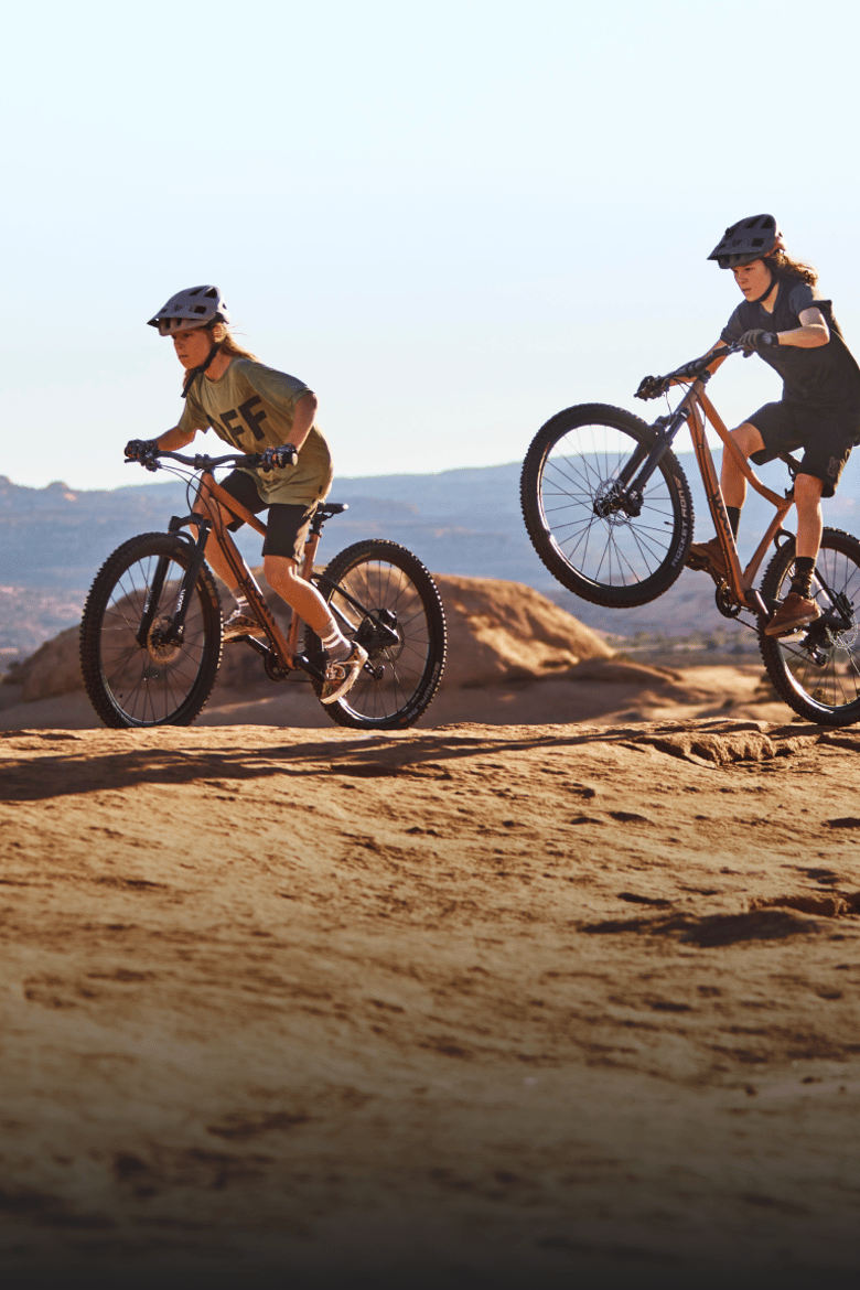 Twee kinderen met fietshelm op fietsen met hun woom OFF AIR mountainbikes over een zandpad in de bergen.
