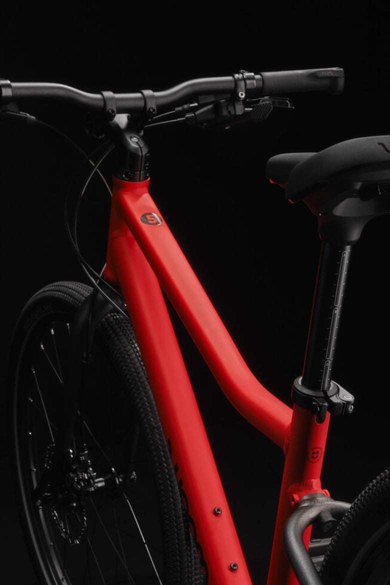 Vue latérale d’un vélo enfant woom EXPLORE avec cadre rouge, logo woom noir et composants noirs.