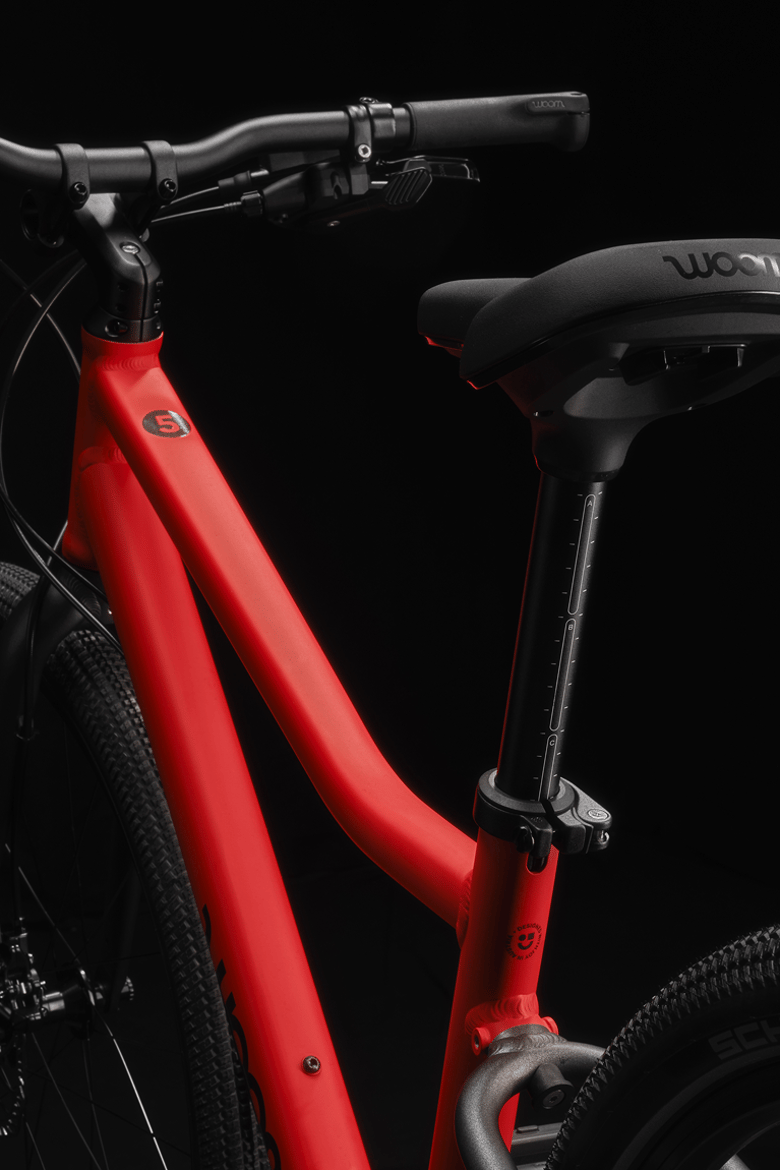 Vélo woom EXPLORE rouge avec guidon, tige de selle, fourche et haubans noirs.