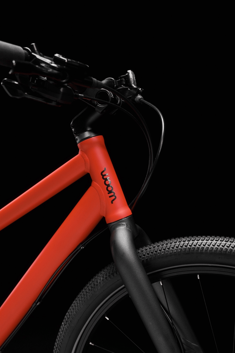 Profil d'un vélo enfant woom EXPLORE rouge avec logo woom noir et composants noirs.