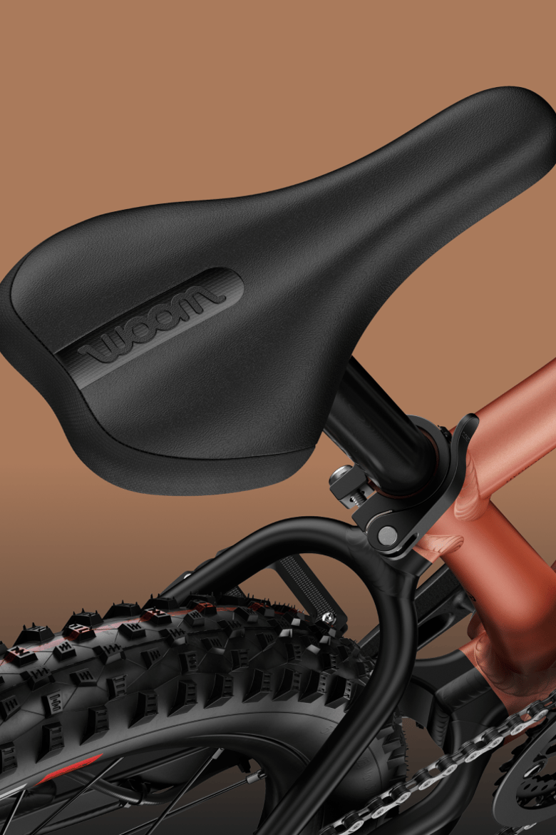 Zoom sur la selle noire et le pneu arrière d'un VTT woom OFF AIR au cadre couleur cuivre.