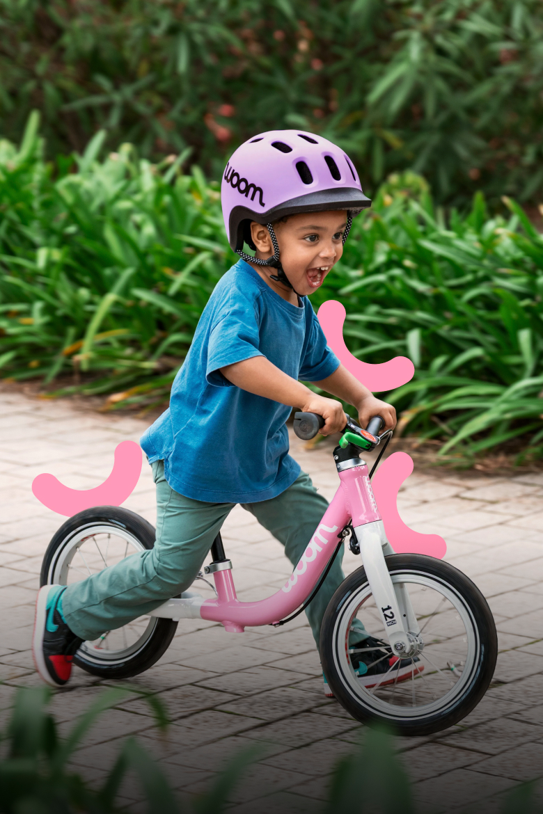 Enfant avec casque woom READY violet roulant joyeusement sur un woom GO 1 rose.