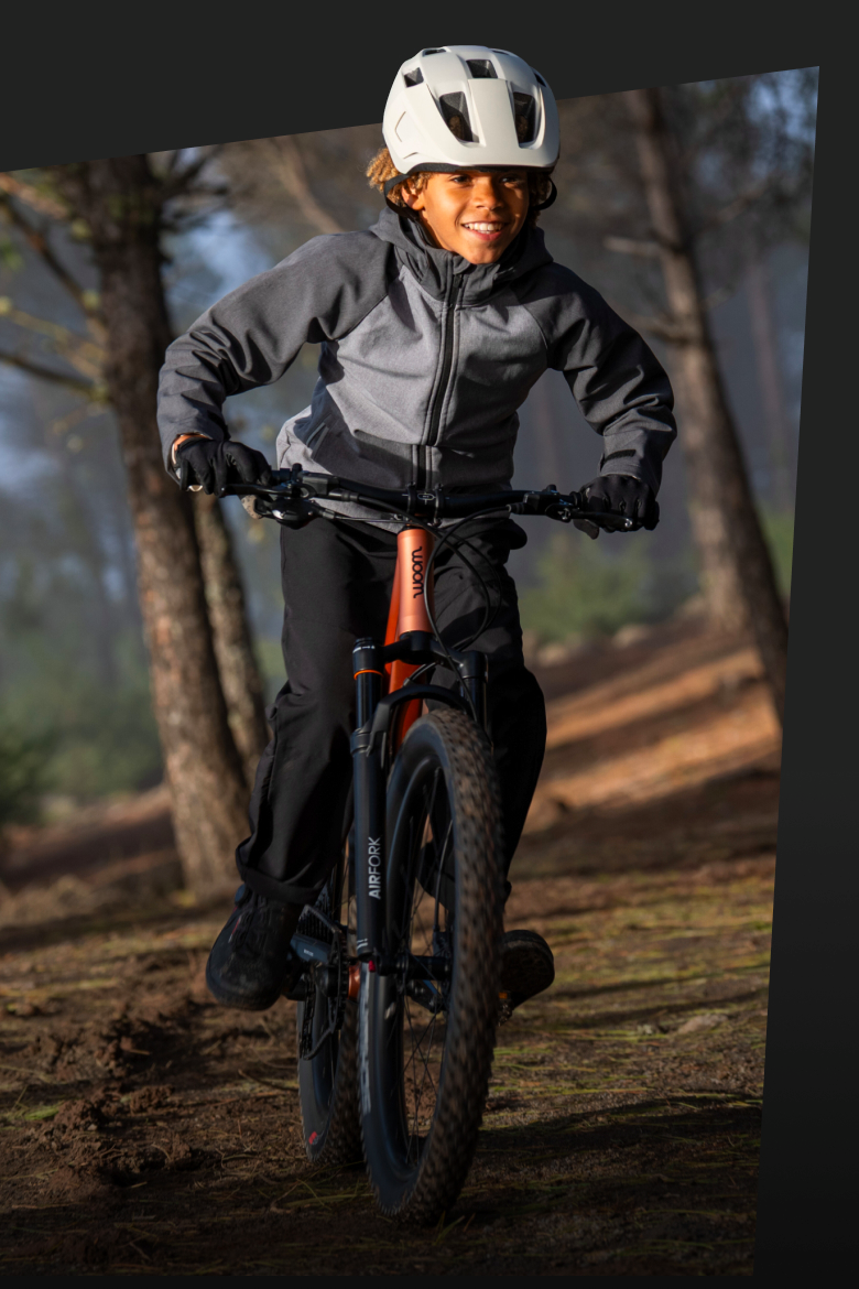 Enfant avec casque woom READY blanc sur un VTT woom OFF en forêt.