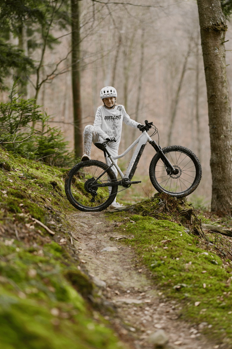 Girl posing with a woom UP e-mountain bike in cirrus cloud on a forest path.