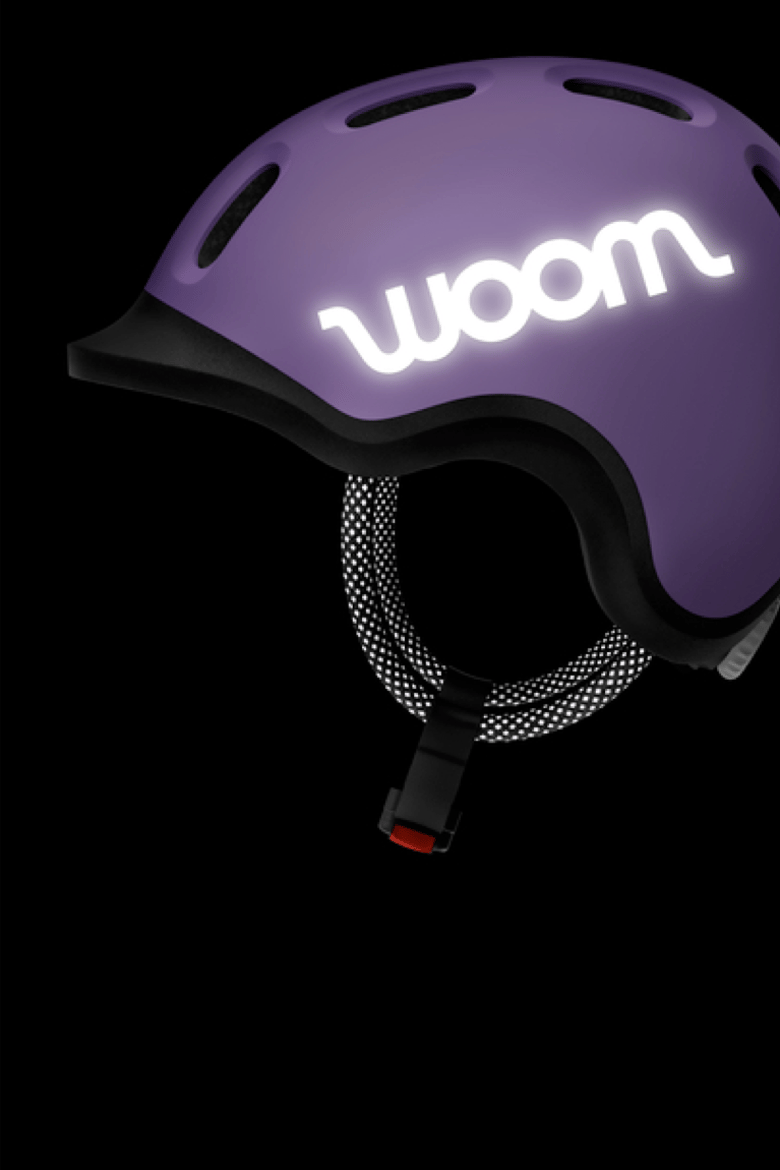 Vue latérale du casque enfant READY de couleur violette dans le noir avec logo woom et cordon réfléchissants