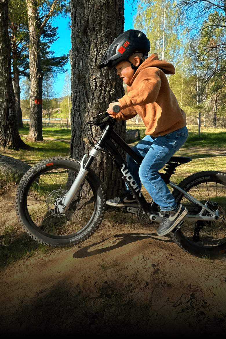 A boy wearing a bike helmet is riding a black woom OFF AIR on a trail in the woods.