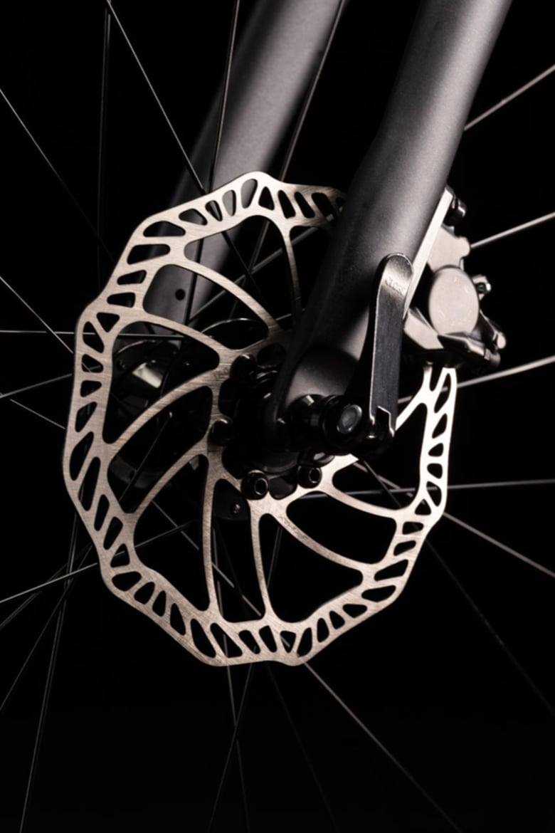 Gros plan d’un disque de frein argenté sur la roue avant d’un vélo enfant woom EXPLORE avec fourche noire.