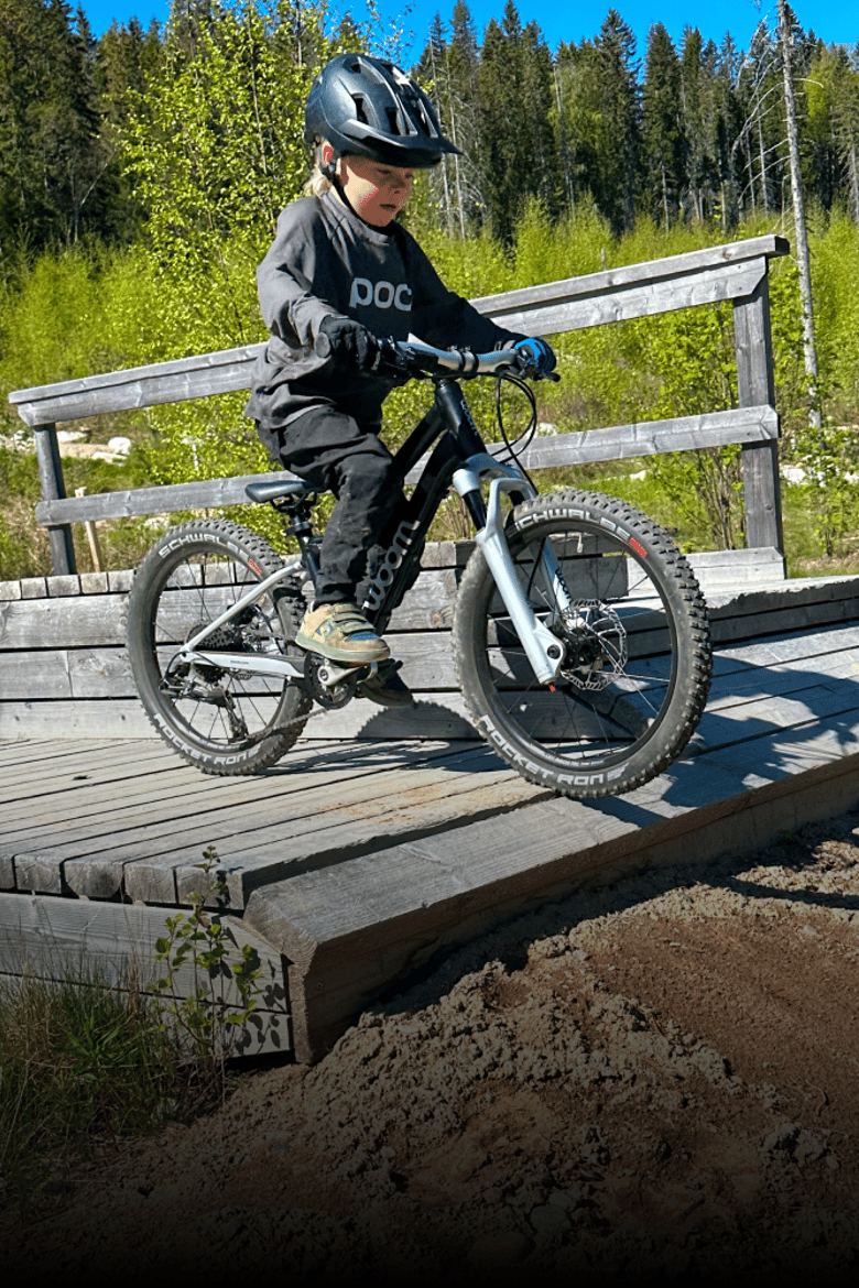 A boy wearing a bike helmet and TENS bike gloves is riding a black woom OFF AIR over a bridge.