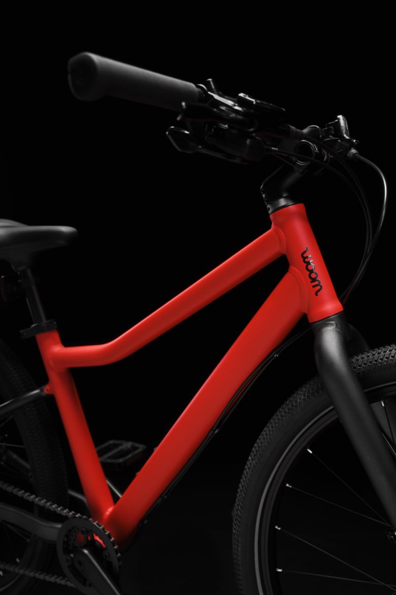 Vélo woom EXPLORE rouge avec guidon noir, tige de selle noire, fourche noire et haubans noirs.