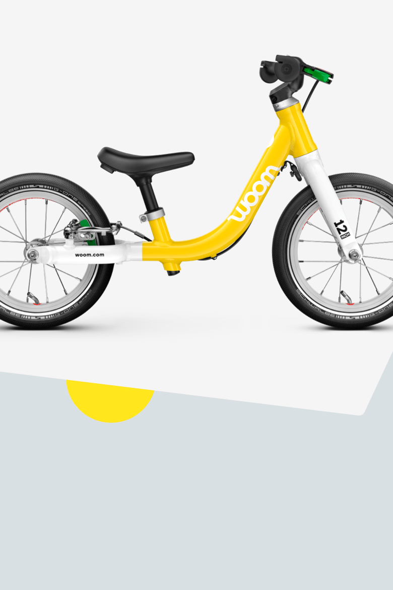 A yellow woom GO 1 balance bike with 12" wheels for children aged approximately 18 months and upwards, viewed from the side