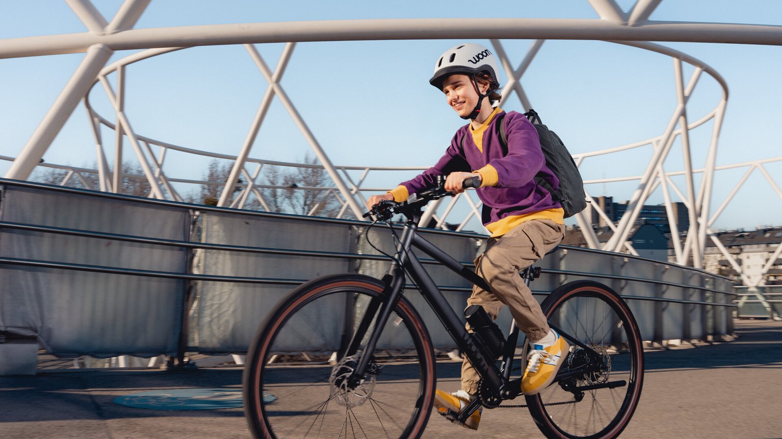 A boy wearing a purple sweatshirt is riding a woom EXPLORE e.