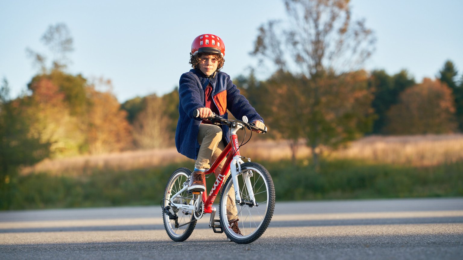 Ein Junge mit rotem woom Helm sitzt auf einem roten woom ORIGINAL 4 Kinderfahrrad in 20 Zoll.