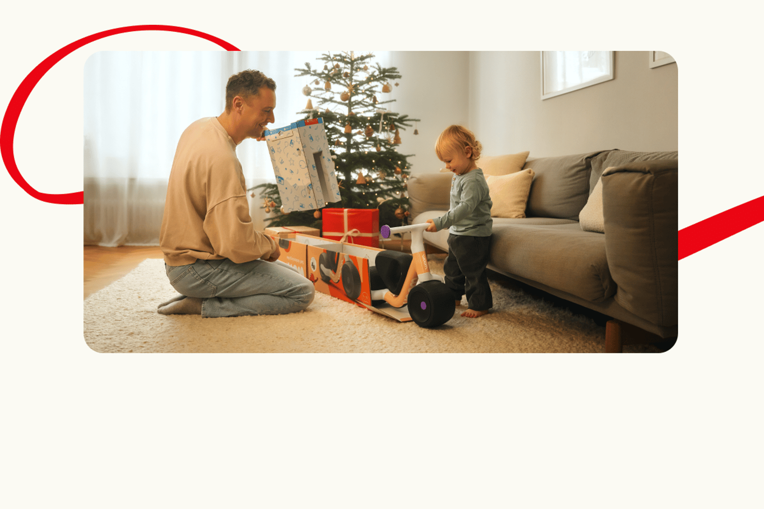 A man and a toddler unboxing a large gift in front of a Christmas tree.