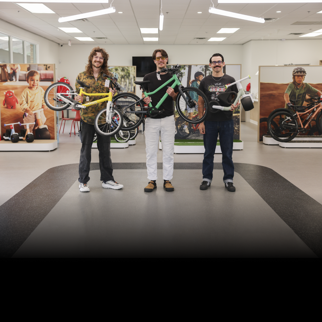 Bike Experts Jackie, Harry, and Matt hold various woom bikes in the showroom.