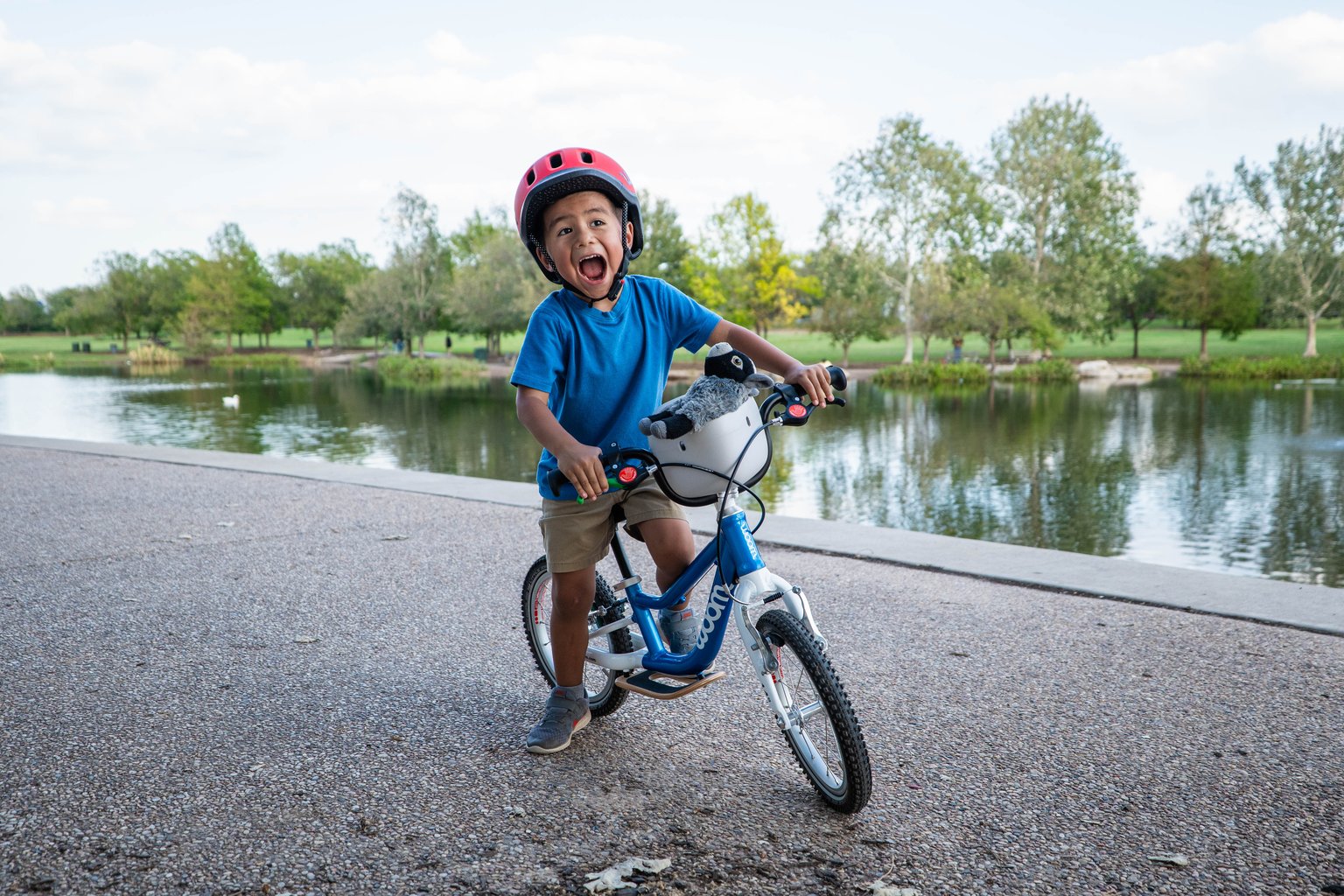 excited kid wearing a red woom READY kids' helmet sitting on a blue woom GO 1 PLUS with a gray POP Basket on it.