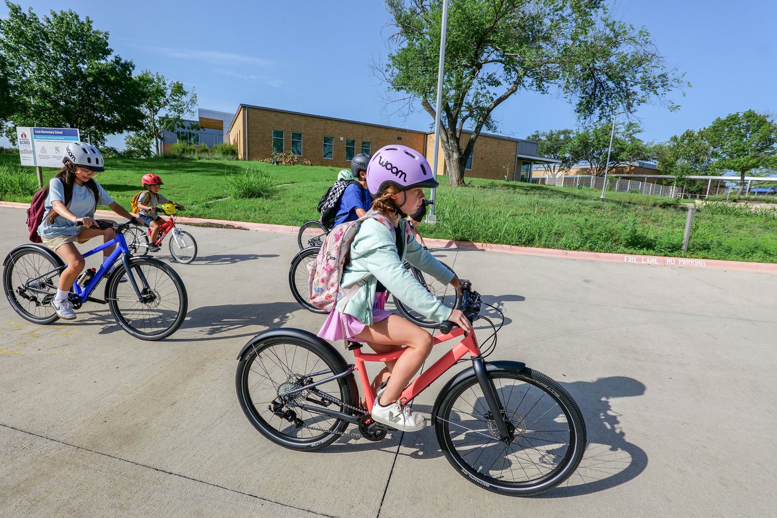 group of kids riding woom EXPLORE bikes to school while wearing woom READY Kids' Helmets and backpacks