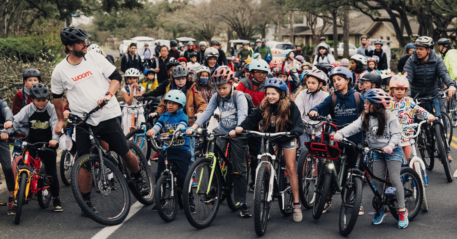 A crowd of kids on bikes lines up at the direction of their chaperone to start their Bike Bus ride on a neighborhood street.