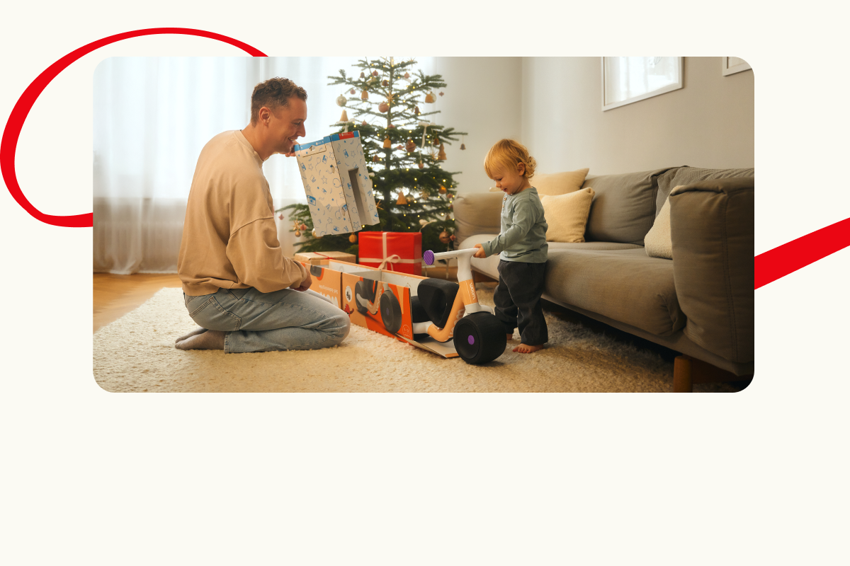 A man and a toddler unboxing a large gift in front of a Christmas tree.