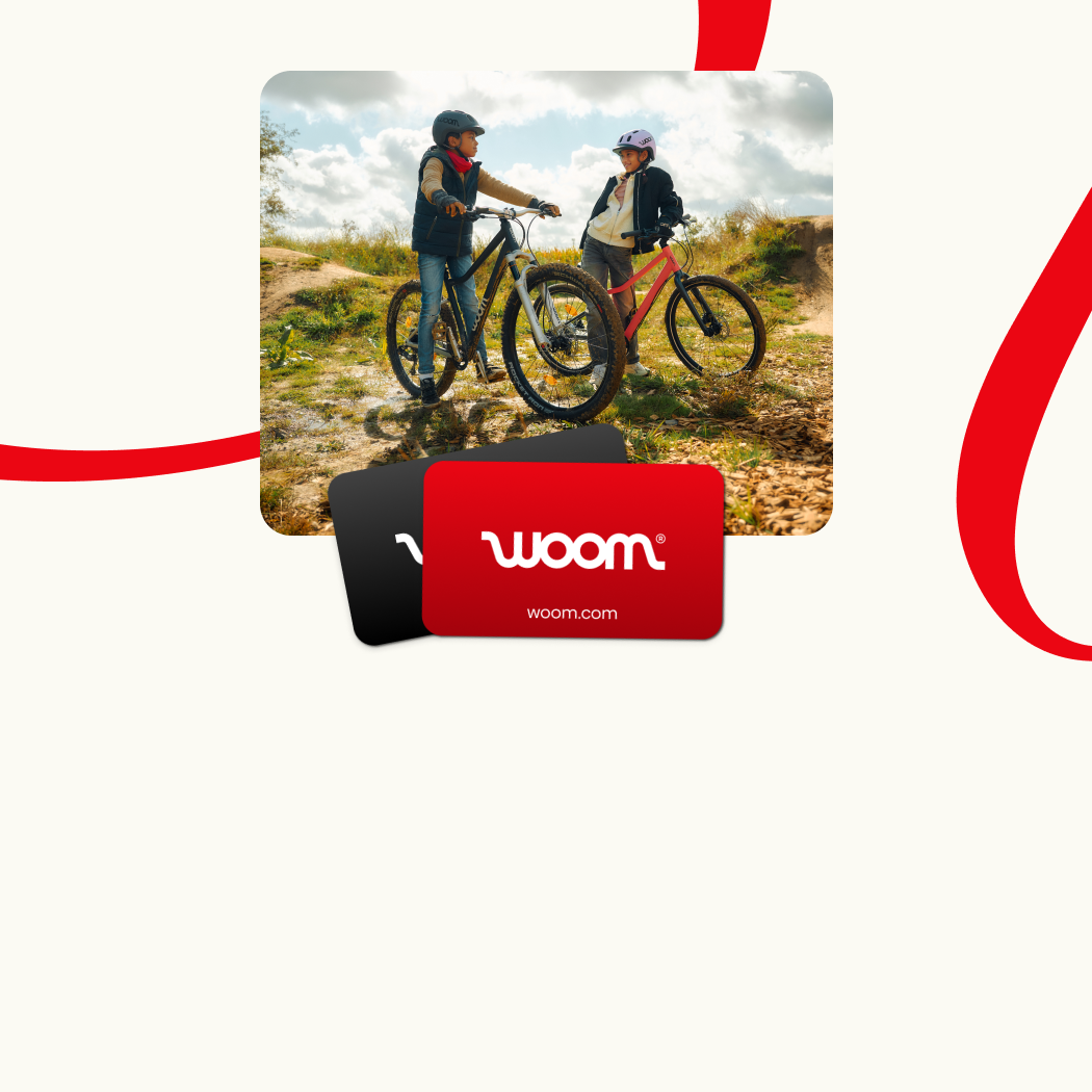 An image featuring two woom gift cards superimposed on a photo of two kids in a hilly outdoor setting. One is on a woom EXPLORE and the other is on a woom OFF, and they are chatting with each other while wearing woom READY Helmets. This is overlaid on a cream-colored background with red ribbons.