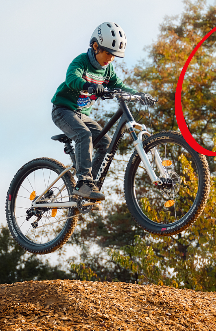 A child with a helmet is jumping over an earth mound with a black woom OFF.