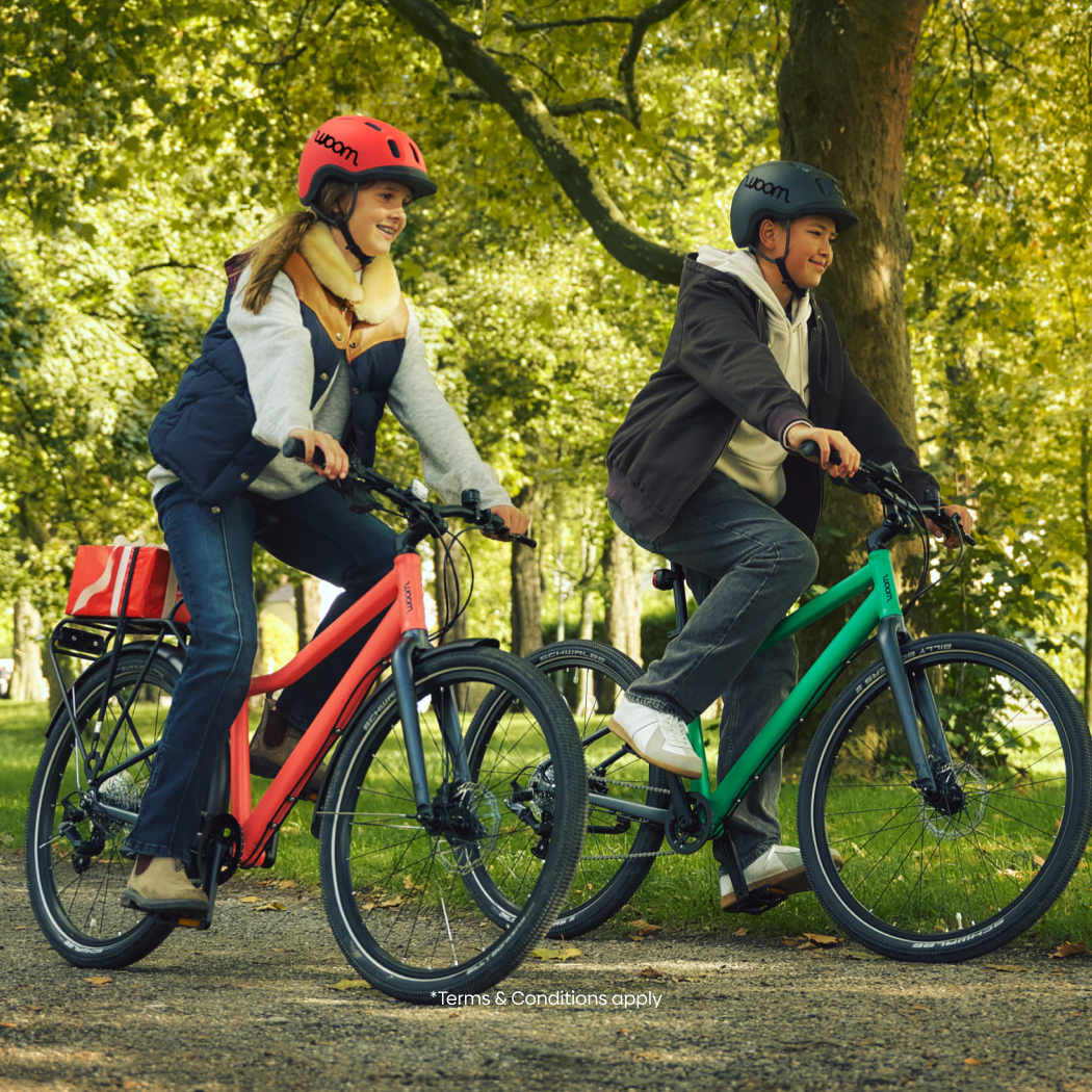 An image of two young teens riding their neon coral and jungle green woom EXPLORE bikes through a bike, overlaid on a cream background with red ribbons