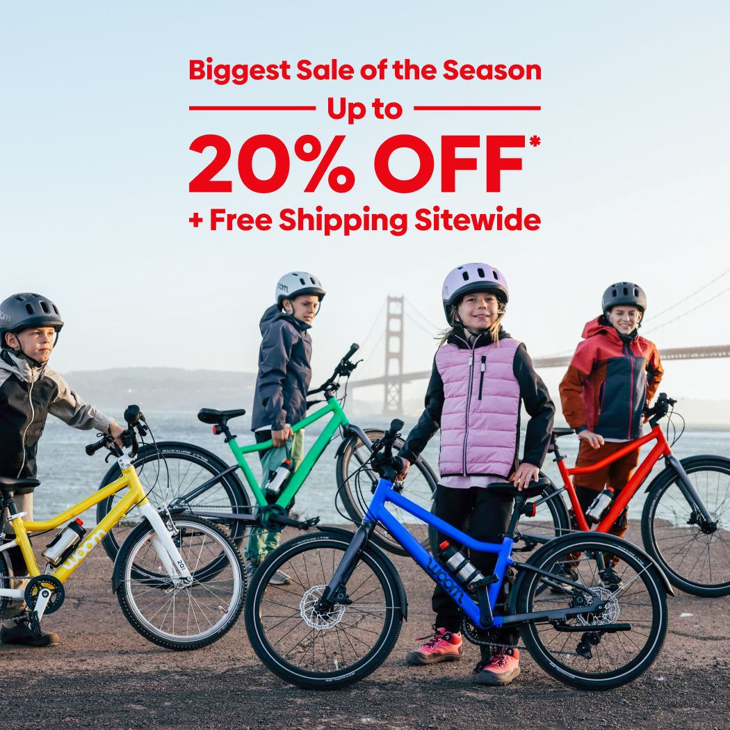 Kids pose with their colorful woom GO and EXPLORE bikes in front of the Golden Gate Bridge on a chilly day. Text over the image reads “Biggest Sale of the Season: Up to 20% Off Plus Free Shipping Sitewide”