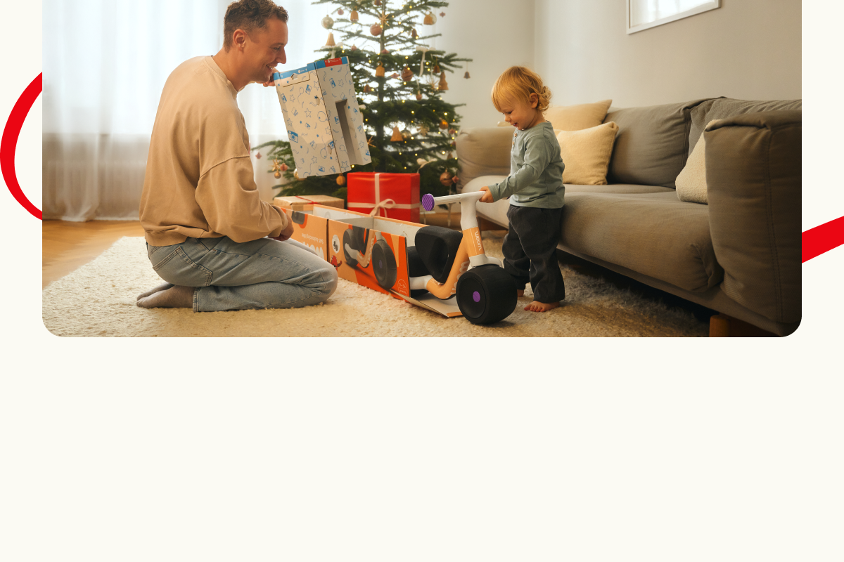Un homme et un enfant en bas âge déballant un gros cadeau devant un sapin de Noël.