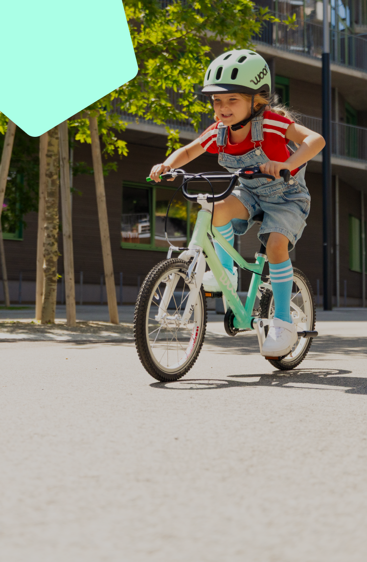 A child in a turquoise READY bicycle helmet rides a limited edition spearmint crush woom GO children's bike.