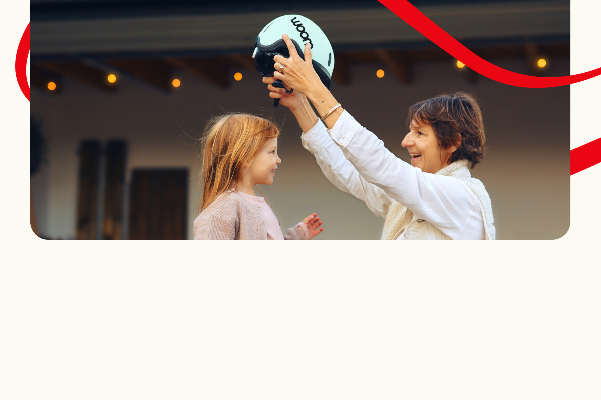 Erwachsener setzt einem Kind einen Helm auf. Dekorative rote Linien im Hintergrund.