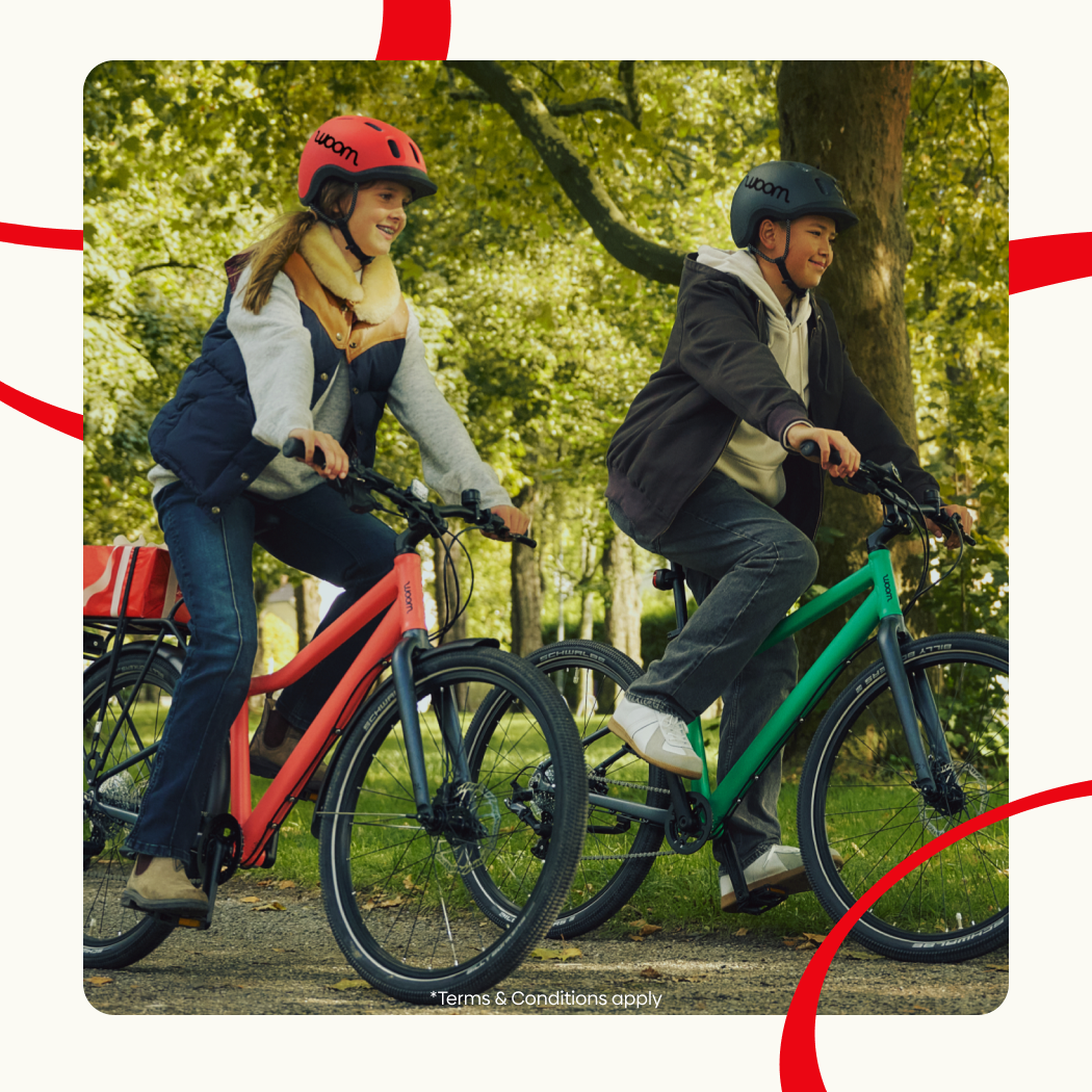 An image of two young teens riding their neon coral and jungle green woom EXPLORE bikes through a bike, overlaid on a cream background with red ribbons