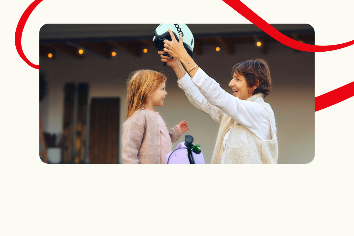 Adult putting a helmet on a child's head. Decorative red lines in the background.