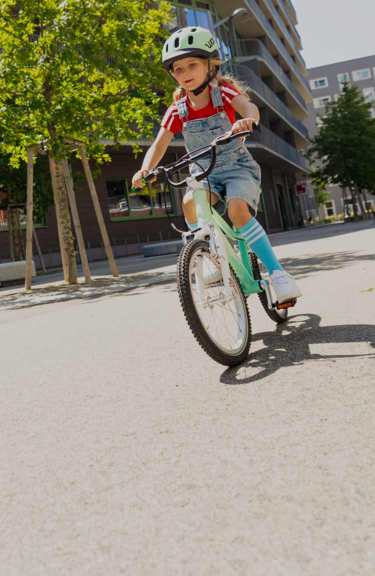 Mädchen mit READY Helm in Mint auf dem Kopf fährt entlang eines Wohnblocks auf dem Fahrrad woom GO in spearmint crush.
